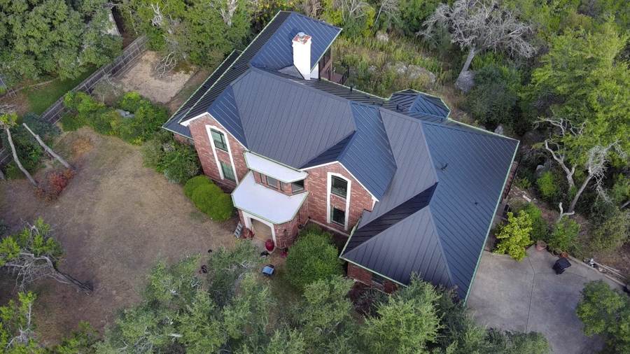 Dark standing seam metal roof on a brick home surrounded by trees