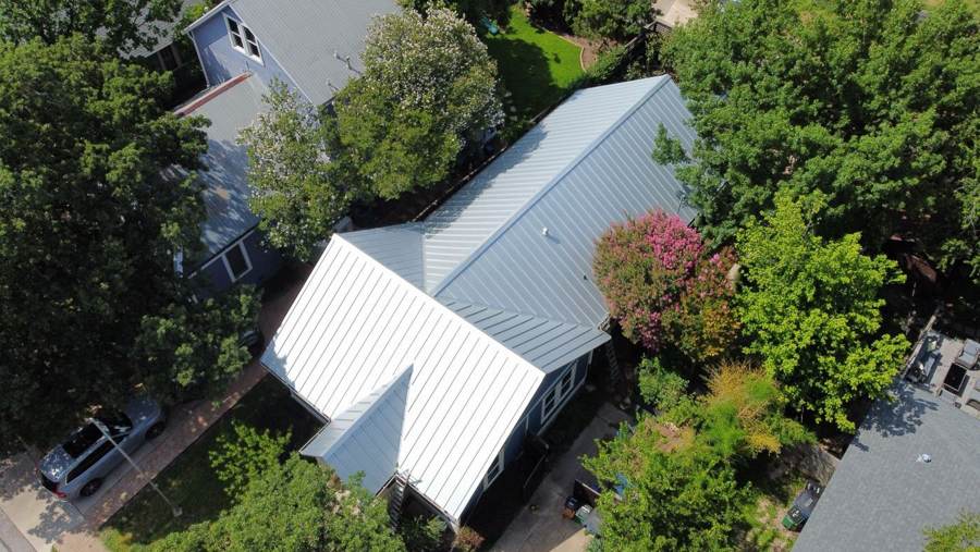 Silver standing seam metal roof on a blue house among trees
