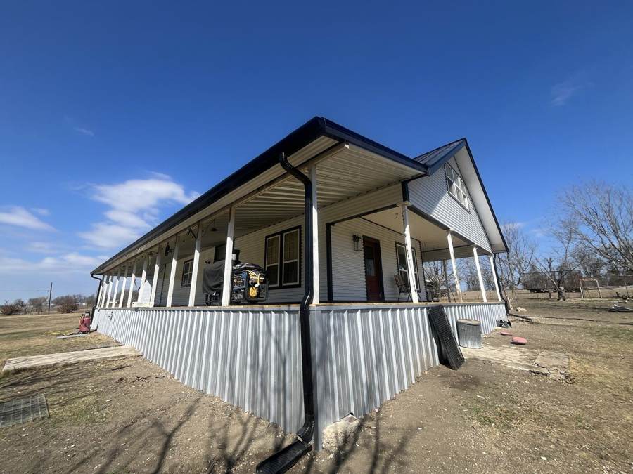 Farmhouse wraparound porch with black gutters and metal skirting